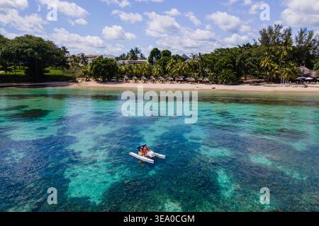 Des aventures en couple sur un kayak au milieu des eaux turquoises époustouflantes de Triolet. Des palmiers luxuriants et des plages de sable créent une toile de fond idyllique pour des vacances romantiques au paradis. Banque D'Images
