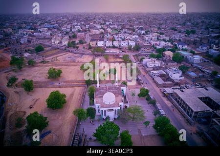 Vue aérienne d'une mosquée blanche avec des minarets jumeaux debout en bonne place au milieu de l'étalement urbain, baignée dans la douce lueur du crépuscule, Kano, Kano, Nigeria. Banque D'Images