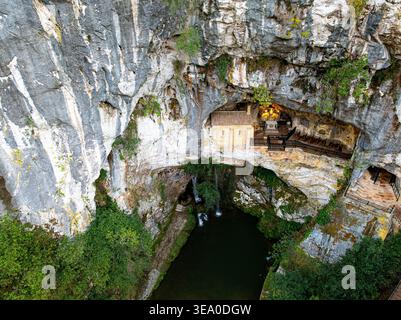 Vue aérienne d'une chapelle sereine nichée dans une grotte, où la lumière danse sur la pierre, créant une ambiance éthérée, Santa Cueva de Covadonga, SP Banque D'Images