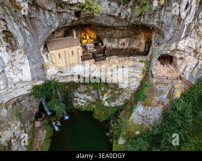 Vue aérienne de la chapelle de pierre accrochée à l'embouchure accidentée de la grotte, un sanctuaire de lumière contre les falaises sombres et spectaculaires, Santa Cueva de Covadonga, S. Banque D'Images