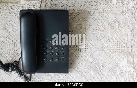 Téléphone fixe filaire noir vintage avec combiné amovible sur nappe en dentelle, concept de communication rétro nostalgique. Orientation horizontale, vue de dessus Banque D'Images