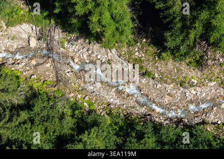Vue aérienne au-dessus du dessus de la vue de montagne ruisseau rocheux lit de rivière dense vert forêt de conifères soleil . L'eau claire coule sur des pierres gravier forme naturelle Banque D'Images