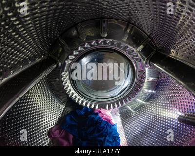 Vue intérieure du tambour de machine à laver avec linge bleu et rose Banque D'Images