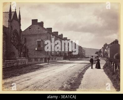 Pensarn, The Street de Francis Bedford, 1860–94, montrant une route de village tranquille bordée de bâtiments en pierre et en ardoise, deux personnages conversant sur le trottoir, et des montagnes visibles au loin Banque D'Images