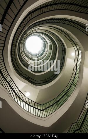 Perspective verticale d'un escalier en colimaçon. Photo en bas angle d'un escalier sinueux avec des balustrades sombres et un puits de lumière lumineux. Banque D'Images