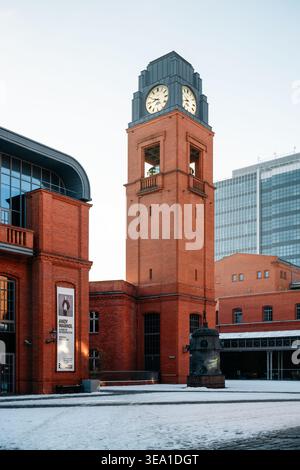 Architecture industrielle de Stary Browar. Un grand plan de la tour de l'horloge en brique rouge avec le dessus en métal foncé le matin d'hiver. Banque D'Images