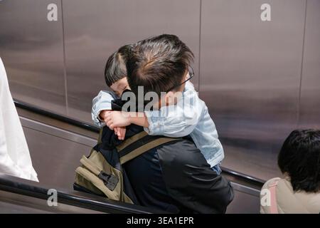 Taipei, Taiwan - 26 décembre 2024 : le père porte sa fille endormie sur son dos sur un escalier roulant MRT de Taipei dans un moment franc et chaleureux. Banque D'Images