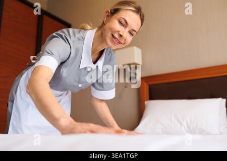 Gros plan de la femme de ménage souriante de l'hôtel qui prépare un lit bien arrangé Banque D'Images