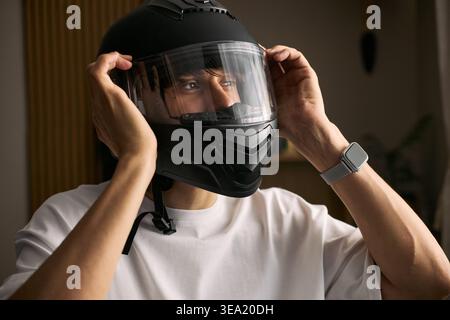 Jeune homme asiatique adulte ajustant le casque de moto avant de rouler, mettant l'accent sur la sécurité routière et la mobilité personnelle. Utile pour l'assurance transport, la formation des cavaliers, les campagnes de navettage Banque D'Images