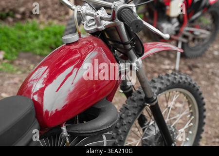 Moto de motocross rouge vintage avec un réservoir de carburant brillant et des pneus hors route Knobby garés sur un sentier de terre, concept de vélo de terre rétro. Banque D'Images