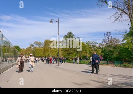 PARIS, FRANCE — 21 AVRIL 2024 : foules de gens marchant le long du mur de sécurité en verre au pied de la Tour Eiffel sur le champ de mars sous une clairière Banque D'Images