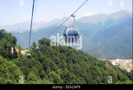 Cabine de téléphérique se déplaçant au-dessus de la forêt verte avec fond de chaîne de montagnes. Banque D'Images