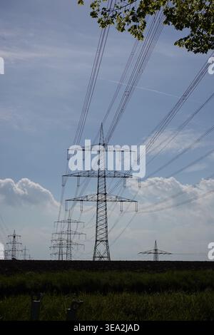 Les lignes électriques hautes tiennent fermement sur le terrain. La lumière du soleil brille sur le paysage tandis que les nuages moelleux dérivent dans le ciel bleu. La scène capture l'essence o Banque D'Images