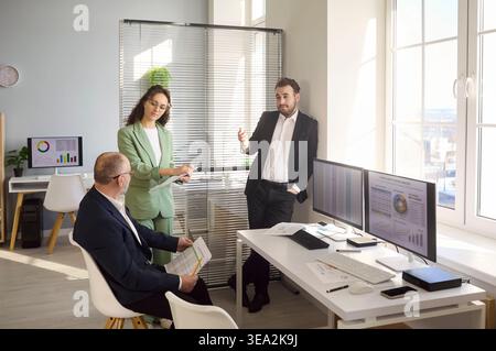 Équipe commerciale discutant de l'analyse par bureau avec des écrans d'ordinateur et des graphiques de données Banque D'Images