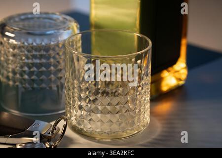 Deux verres à gobelet avec un à l'envers et un face vers le haut avec un ensemble de clés de voiture et une bouteille de whisky en arrière-plan floue sur une surface sombre Banque D'Images