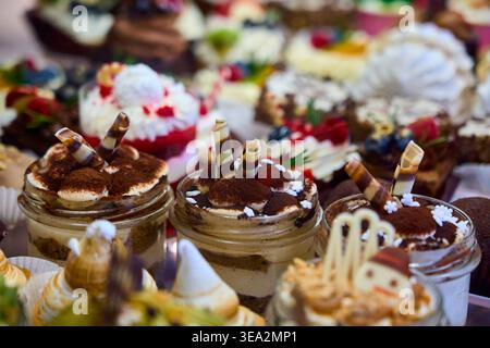 Assortiment de mini desserts dans des bocaux en verre et pâtisseries sur un présentoir. Tiramisu avec des petits pains au chocolat et des gâteaux crémeux aux baies. Buffet sucré. Banque D'Images
