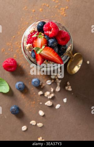 Plan haut vers le bas d'un pot en verre rempli de couches de granola et de framboises fraîches, fraises et bleuets. Une lumière naturelle douce met en valeur le tex Banque D'Images