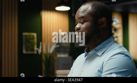 Portrait d'homme d'affaires noir fait la pensée critique et la relecture des fichiers avant de transcrire les données sur ordinateur portable, assis dans le bureau la nuit. Documenter les idées importantes heures supplémentaires. Banque D'Images
