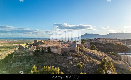 Une vue aérienne évocatrice du château de Sagunto baignée par la lumière du coucher de soleil. L'image met en évidence les vastes fortifications et bastions que domi Banque D'Images