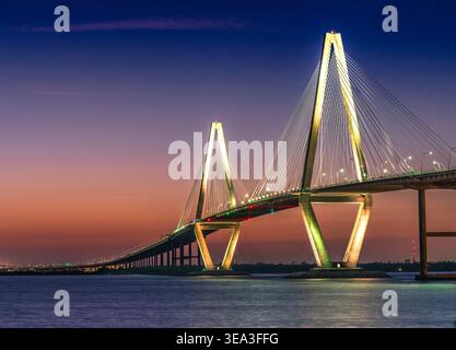 Charleston, Caroline du Sud - US - 27 mars 2026 Twilight s'installe au-dessus de l'Arthur Ravenel Jr. Pont, ses câbles lumineux reflétant à travers les eaux calmes du port Banque D'Images
