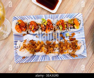 Sur la table, il y a une assiette avec un ensemble de sushi - rouleaux uramaki avec concombre, crabe avocat et saumon Banque D'Images