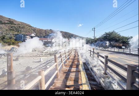 Les vues spectaculaires de Unzen Jigoku au Japon présentent une épaisse vapeur de soufre, un terrain géothermique rocheux et des passerelles en bois dans un ciel bleu clair. Banque D'Images