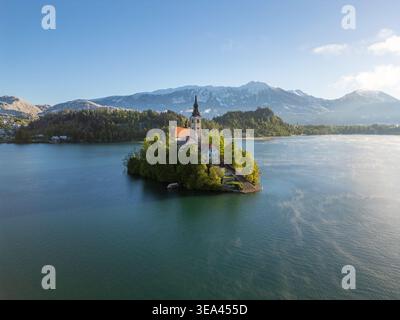 Vue aérienne de l'église de pèlerinage de l'Assomption de Marie sur l'île de Bled, entourée d'eau bleue calme et de montagnes enneigées à Bled, Radovl Banque D'Images
