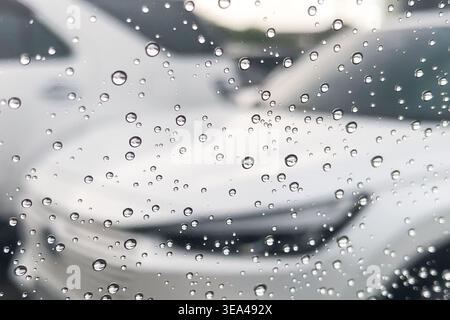 Gouttes de pluie sur la fenêtre de la voiture, voitures blanches floues dans le fond. Banque D'Images