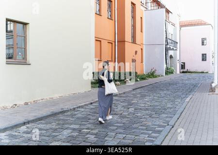 femme marchant le long de la rue pavée colorée avec sac fourre-tout dans la zone urbaine calme Banque D'Images