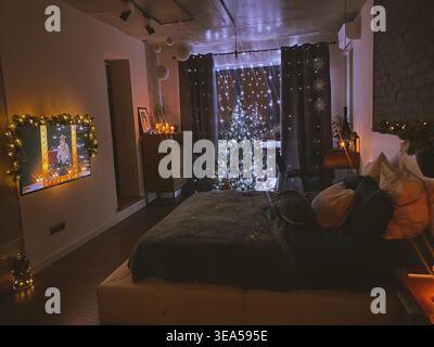 Intérieur de chambre confortable décoré pour Noël avec arbre illuminé, lumières chaudes, bougies et décorations festives créant une atmosphère hivernale calme. Banque D'Images