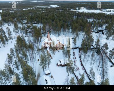 Vue aérienne du bâtiment principal du village du Père Noël entouré de forêts de pins enneigées et de structures traditionnelles en bois à Rovaniemi, Laponie, Finl Banque D'Images