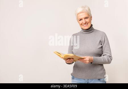 Femme senior lisant un livre tout en souriant et en profitant de son temps calme à l'intérieur Banque D'Images