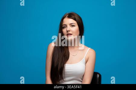 Jeune femme posant dans un studio avec un fond bleu vif, mettant en valeur sa beauté naturelle et son expression authentique Banque D'Images
