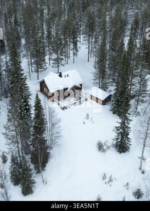 Vue aérienne d'une cabane traditionnelle en bois nichée parmi les pins enneigés dans une forêt d'hiver en Laponie, Finlande. Banque D'Images