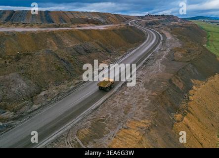 La vue aérienne montre un gros camion à benne basculante transportant des matériaux sur un large chemin de terre sur un site minier à ciel ouvert pendant la journée Banque D'Images