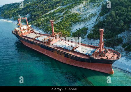 Vraquier échoué reposant sur une rive rocheuse à côté d'une colline boisée verte vibrante pendant la journée Banque D'Images