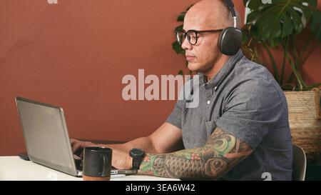 Homme professionnel focalisé travaillant sur ordinateur portable avec casque dans le bureau à domicile moderne Banque D'Images