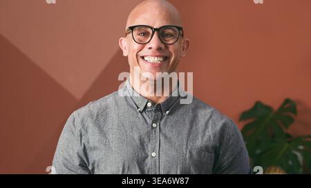 Homme chauve professionnel souriant portant des lunettes et une chemise décontractée boutonnée dans le portrait de bureau Banque D'Images