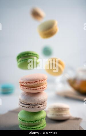 gros plan de macarons français pastel empilés sur une table neutre avec des macarons colorés supplémentaires suspendus en plein air ; lumière naturelle douce, faible profondeur Banque D'Images