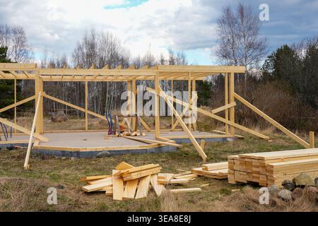 Ossature de maison en bois en cours avec planches empilées et outils sur un chantier de construction de campagne Banque D'Images