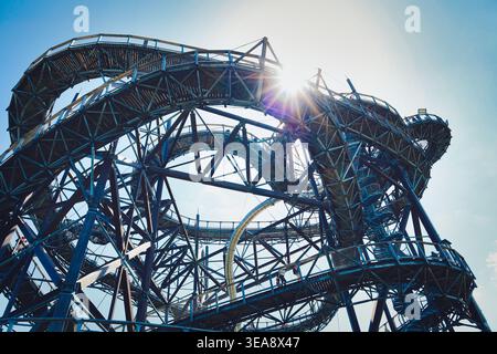 Vue en bas angle d'une passerelle d'observation moderne en acier avec des courbes torsadées, des éruptions de soleil et un ciel bleu clair ; architecture industrielle, repère urbain, tra Banque D'Images