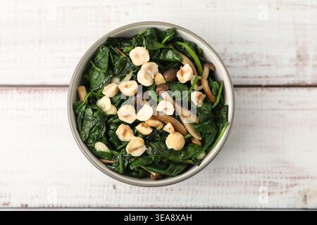 Savoureux épinards sautés avec champignons shimeji, noisettes et ail sur table en bois clair, vue de dessus Banque D'Images