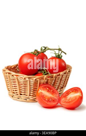 Petit panier en osier rempli de tomates de brousse entières (lat : Solanum lycopersicum) et une tomate coupée en deux sur un fond blanc de studio avec des ombres. Banque D'Images