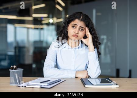 Jeune femme se sentant accablée et stressée par le travail, souffrant d'un mal de tête et d'épuisement professionnel alors qu'elle était assise à son bureau dans un lieu de travail contemporain professionnel Banque D'Images