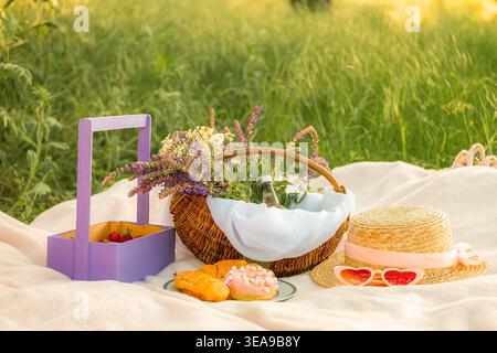 Deux croissants et un beignet reposent sur une plaque bleue avec un rebord doré sur une couverture blanche. À côté se trouve un chapeau de paille et des verres en forme de coeur, panier avec daisi Banque D'Images