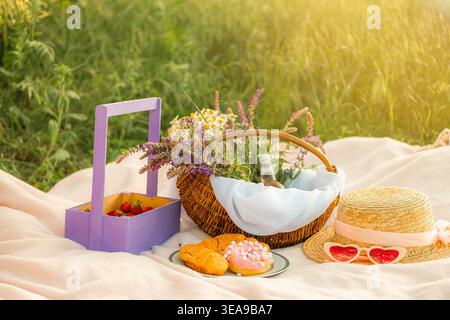 Deux croissants et un beignet reposent sur une plaque bleue avec un rebord doré sur une couverture blanche. À côté se trouve un chapeau de paille et des verres en forme de coeur, panier avec daisi Banque D'Images