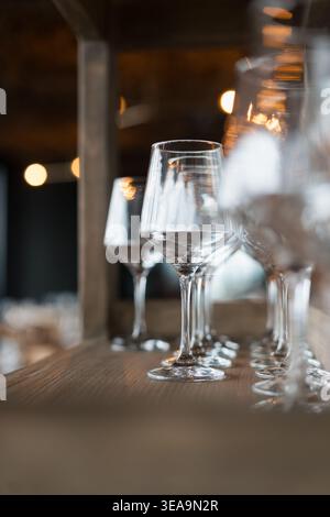 Verres à vin clairs se tiennent dans une rangée sur une table en bois. Les lumières douces rendent l'arrière-plan flou. La mise au point est nette sur les lunettes de premier plan. Ambiance chaleureuse suggère Banque D'Images