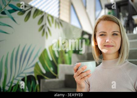 Femme tenant une tasse de café, souriant à l'intérieur, murale tropicale Banque D'Images