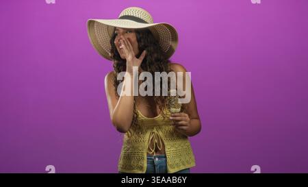 Femme hispanique tient un popsicle saupoudré, main à bouche murmure dans le studio ; vibes d'été secrètes et ludiques. Banque D'Images