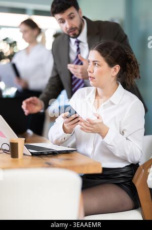 Un patron masculin gronde une employée pour avoir fait défiler son smartphone tout en travaillant au bureau Banque D'Images